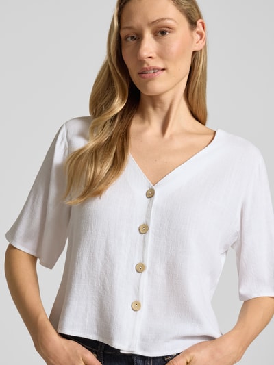 Frauenmodel trägt Hemdbluse aus Viskose-Mix mit Leinen-Anteil von Apricot in Weiß, gerader Schnitt, V-Ausschnitt, Knopfleiste, Nahaufnahme Oberkörper.