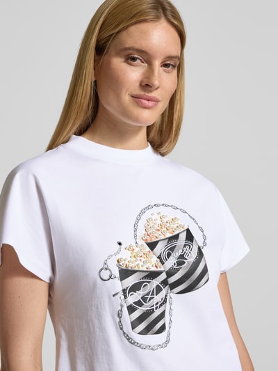 Frauenmodel trägt Regular Fit T-Shirt mit Ziersteinbesatz Modell 'Popcorn' von Guess, Weiß mit Print und Rundhalsausschnitt, Nahaufnahme Oberkörper.