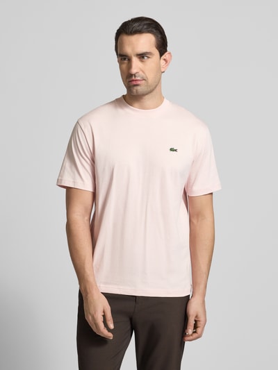 Mannelijk model draagt Regular Fit T-Shirt aus reiner Baumwolle van Lacoste, effen lichtroze, label stitching, logo-patch, ronde hals, korte mouw, puur katoen, standaardpasvorm. Halffiguur vooraanzicht.