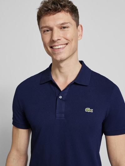 Męski model nosi Slim Fit Poloshirt aus reiner Baumwolle od Lacoste, jednolity kolor, wyhaftowane logo, kołnierzyk polo, krótki rękaw, pika, bawełna, zbliżenie na górną część ciała