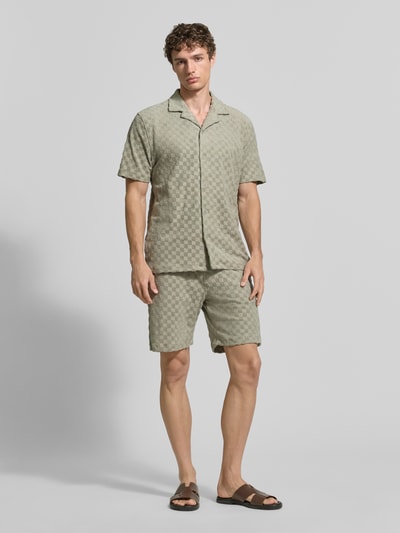 Męski model nosi Regular Fit Freizeithemd mit Reverskragen von Lindbergh, mieszanka bawełny, listwa guzikowa, długość tyłu w rozmiarze M: 73 cm, szerokość ramion w rozmiarze M: 48 cm, długość rękawów w rozmiarze M: 27 cm, jasny wzór w kratę, miękka tekstura, całkowity widok z przodu.