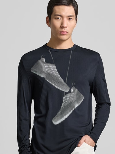 Männermodel trägt Regular Fit Longsleeve mit Motiv-Print von MM6 Maison Margiela in Schwarz mit Strukturmuster, Rundhalsausschnitt, Nahaufnahme Oberkörper.