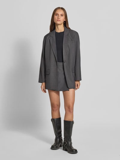 Modelka nosi szarą spódnicę mini Regular Fit Skort mit Gürtelschlaufen model 'LINDA' od ONLY, czarną koszulkę i szary żakiet, kontekst: damska spódnica mini od ONLY, widok całej sylwetki z przodu.