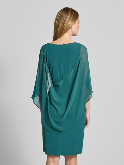 Modelka nosi Knielanges Cocktailkleid mit Rundhalsausschnitt von Vera Mont, elastyczna mieszanka materiałów, dopasowany krój, okrągły dekolt, kopertowy styl, ozdobna aplikacja z obszyciem z kamieni stras, długość do kolan, wszyty zamek błyskawiczny z tyłu, rękawy nietoperzowe z szyfonu, długość tyłu w rozmiarze 36: 98 cm, szerokość w rozmiarze 36: 108 cm, długość rękawów w rozmiarze 36: 48 cm, widok całej sylwetki z tyłu.
