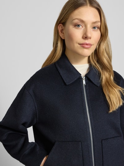 Vrouwenmodel draagt Jacke aus Lanawoll-Mix Modell 'Hilvyn' van OPUS in donkerblauw, relaxed fit, platte kraag, tweewegritssluiting, borstwijdte 68 cm bij maat 36, mix van lanawol en viscose, ruglengte 59 cm, schouderbreedte 51 cm, mouwlengte 55 cm, detailopname bovenlichaam.