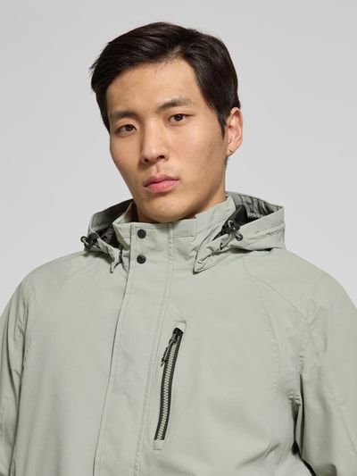Männermodel trägt Jacke mit Napoleontasche Modell 'KOS' von Killtec in Hellgrau, Kapuze mit Tunnelzug, Nahaufnahme Oberkörper.
