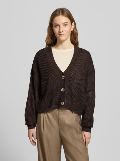 Frauenmodel trägt Regular Fit Strickjacke mit einreihiger Knopfleiste Modell 'CAROL NICE' von Only in Dunkelbraun, unifarben, Strickoptik, tiefer V-Ausschnitt, lange Ärmel, cropped, mit Label Stitching, gerippte Abschlüsse, Ganzkörperansicht von vorne.