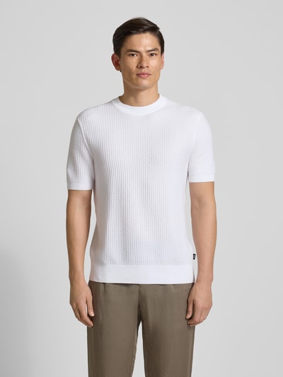 Männermodel trägt Regular Fit Strick-Shirt aus reiner Baumwolle Modell 'H-NILTON' von BOSS in Weiß mit Strukturmuster, Ganzkörperansicht von vorne.