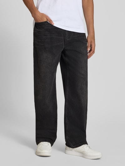 Męski model nosi Baggy Jeans in schwarzer Waschung und klassischem 5-Pocket-Design von REVIEW, Mieszanka bawełny i elastanu, krój baggy, czarny kolor, zapięcie na guzik i zamek błyskawiczny, szerokość w rozmiarze 32: 42 cm, długość wewnętrzna nogawki w rozmiarze 32: 76 cm, stylizowana na denim, całkowita sylwetka z przodu.