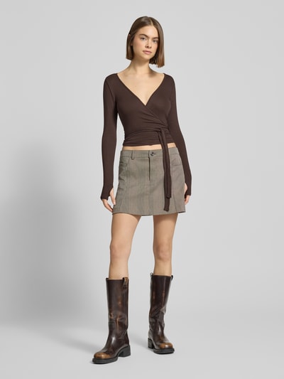 Frauenmodel trägt Slim Fit Longsleeve aus Viskose-Mix Modell 'Soft' von Gina Tricot in Wickel-Optik, V-Ausschnitt, braun, Ganzkörperansicht von vorne.