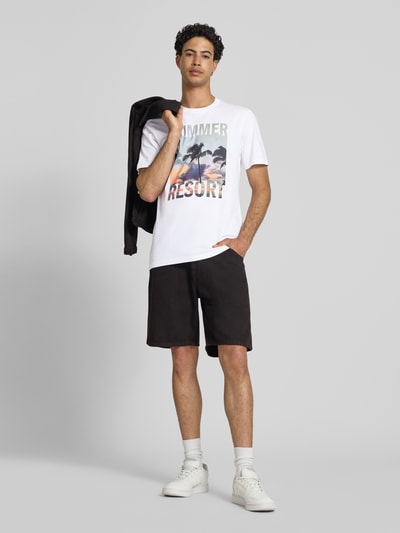 Männermodel trägt Regular Fit T-Shirt aus reiner Baumwolle Modell 'MAGDY LIFE' von Only & Sons, Optik: unifarben, Applikation: Foto-Print, Rundhals, Ärmelform: kurzarm, Material: reine Baumwolle, Farbkombination aus Weiß und Schwarz, glatte Textur, Ganzkörperansicht von vorne.