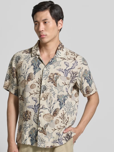 Männermodel trägt Regular Fit Freizeithemd aus reinen Leinen von Gant mit Allover-Motiv-Print, Reverskragen, Logo-Stitching, Kurzärmelig, Knopfleiste und Brusttasche in Naturtönen mit blauen und braunen Akzenten, Textur fein und grob gemustert, Ganzkörperansicht von vorne.