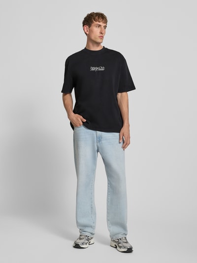 Mannenmodel draagt Oversized T-shirt met Label-Print model 'Ramon' van PEGADOR in zwart, puur katoen, ronde hals, ruglengte maat M 70 cm, oversized fit, labelprint vooraan, lichte structuur, eenvoudige kleuren, full-body vooraanzicht.