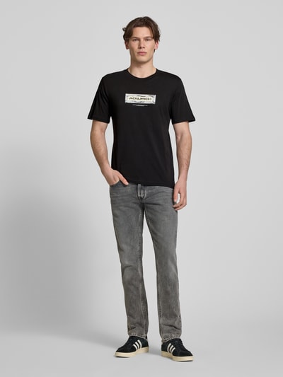 Männermodel trägt T-Shirt mit Logo und Rundhalsausschnitt von Jack & Jones, schwarz, Regular Fit aus Baumwolle, Ganzkörperansicht von vorne.