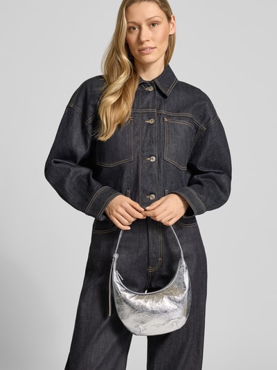 Vrouwenmodel draagt Shoulder Bag met verstelbare schouderriem Model 'Ryker' van LIEBESKIND BERLIN in zilver, logo-reliëf, frontale buste close-up.