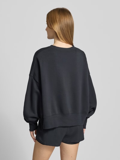 Frauenmodel trägt schwarzes Sweatshirt mit Logo Modell 'Phoenix' von Nike aus Baumwoll-Elasthan-Mix, Regular-Fit, Rundhalsausschnitt, Rückansicht.