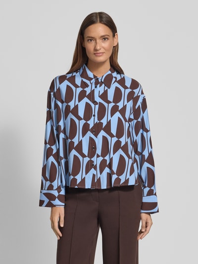Modelka nosi Bluzka koszulowa z mieszanki wiskozy z kołnierzykiem koszulowym Model 'Fetro' od OPUS, krój relaxed fit, długi rękaw, geometryczny nadruk na całej powierzchni, całościowa listwa guzikowa, sportowe mankiety, niebiesko-brązowe kolory, tekstura gładka, długość tyłu 63 cm, długość rękawa 54 cm, widok całej sylwetki z przodu.