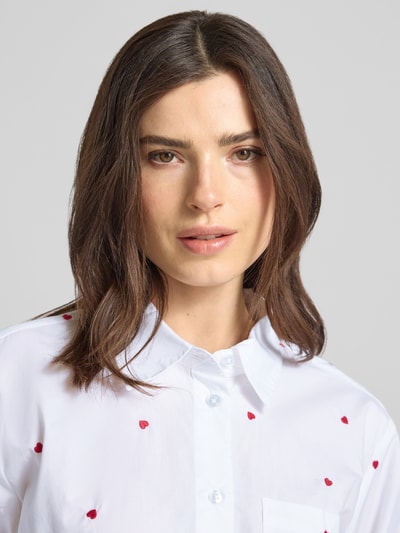 Frauenmodel trägt Boxy Fit Hemdbluse aus reiner Baumwolle von Tom Tailor Denim, weiß mit roten Herzstickereien, Nahaufnahme Oberkörper.