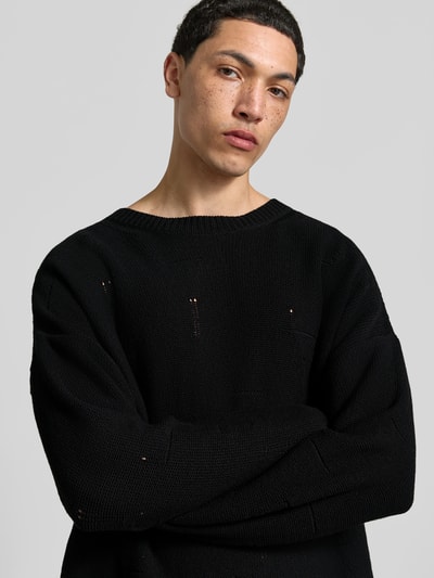 Männermodel trägt Relaxed Fit Pullover im Used-Look von MM6 Maison Margiela aus reiner Baumwolle in Strick-Optik, schwarze Farbe, Nahaufnahme Oberkörper. Rückenlänge bei Größe M: 83 cm.