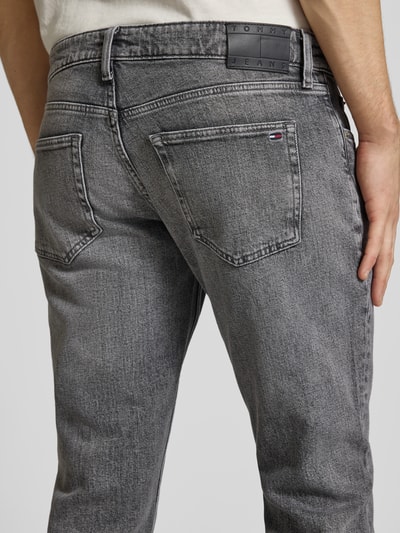Männermodel trägt Slim Fit Jeans aus Baumwoll-Mix Modell 'SCANTON' von Tommy Jeans, grauer Denim, Label Patch, 5-Pocket, Detailaufnahme Rückansicht.
