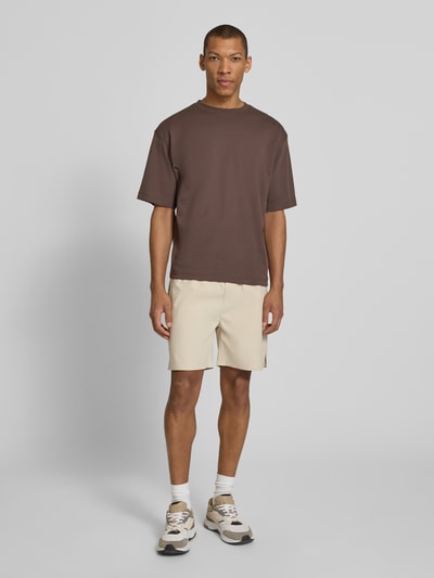 Männermodel trägt Shorts mit elastischem Bund Modell 'Raphael' von Les Deux in Beige mit Regular-Fit und Stretch-Anteil, Material-Mix, Ganzkörperansicht von vorne.
