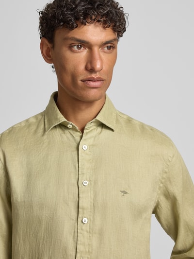 Męski model nosi Slim Fit Leinenhemd mit Haifischkragen od Fynch-Hatton, len, krój slim fit, wyhaftowane logo, kołnierzyk typu cutaway, długość tyłu w rozmiarze M 77 cm, szerokość w rozmiarze M 47 cm, długość rękawów w rozmiarze M 61 cm, jasna zieleń, faktura lnu, bliska perspektywa górnej części ciała.