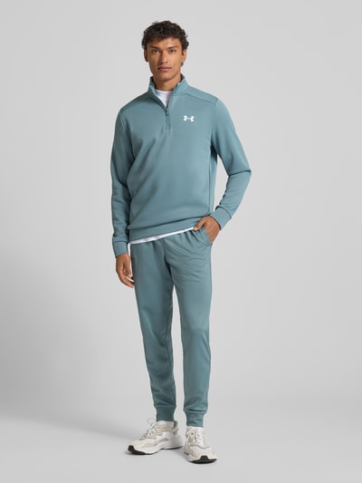 Männermodel trägt Sweatshirt mit Label-Detail von Under Armour in Blau mit Stehkragen, kurzem Reißverschluss, gerippten Abschlüssen, Lockerer-Schnitt, Rückenlänge 72 cm, Ärmellänge 67 cm, Ganzkörperansicht von vorne.