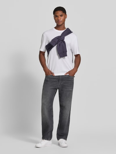 Männermodel trägt Regular Fit T-Shirt aus reiner Baumwolle von Lacoste in Weiß, kombiniert mit lässiger Jeans, Ganzkörperansicht von vorne. Herren T-Shirt von Lacoste.