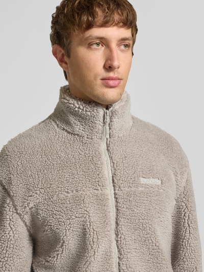Männermodel trägt Fleecejacke mit Label-Detail und Reißverschluss von REVIEW in hellgrauem Teddyfell, Nahaufnahme Oberkörper, Regular Fit. Rückenlänge 70 cm, Schulterbreite 56 cm, Brustweite 59 cm, Ärmellänge 64 cm.