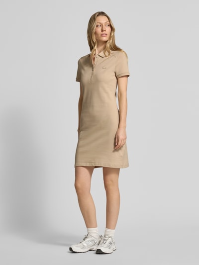 Frauenmodel trägt Slim Fit Polokleid aus Baumwoll-Mix von Lacoste in Unifarben, Mini-Länge, Logo-Stitching, kurze Knopfleiste, Ganzkörperansicht von vorne.