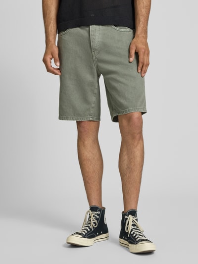 Männermodel trägt Regular Fit Jeansshorts aus reiner Baumwolle Modell 'EDGE' von Only & Sons in grüner Denim-Optik mit Nieten, Label-Patch, 5-Pocket-Design und Knopf mit verdecktem Reißverschluss, Material reine Baumwolle, Nahaufnahme Oberschenkel.