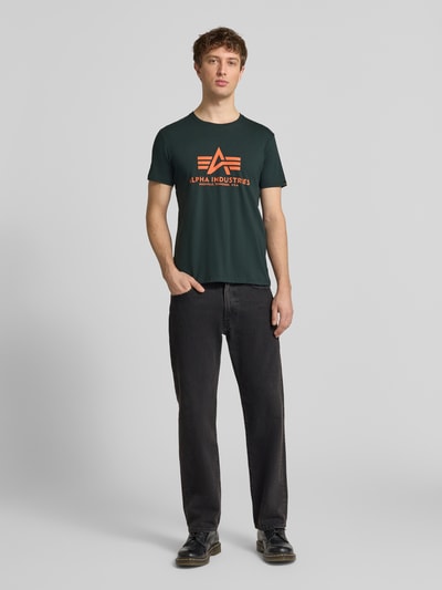 Männermodel trägt T-Shirt mit Label-Detail Modell 'BASIC' von Alpha Industries aus reiner bawełna, prosty krój, okrągły dekolt, długość tyłu w rozmiarze M: 69 cm, Ganzkörperansicht von vorne.
