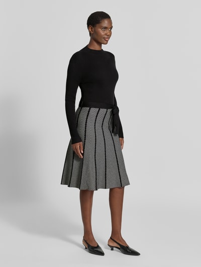 Modelka nosi Knielanges Kleid im 2-in-1-Look od Apricit, mieszanka wiskozy, linia a, długość do kolan, wiązany pasek, długość tyłu w rozmiarze S: 105 cm, szerokość w rozmiarze S: 39 cm, długość rękawów w rozmiarze S: 64 cm, czarno-białe kolory, prosty wzór, tekstura dzianinowa, efekt 2 w 1, widok całej sylwetki z przodu.