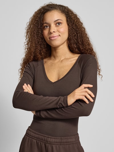 Vrouwenmodel draagt Slim Fit Longsleeve met V-hals van Gina Tricot in bruine katoenmix, dames shirt met lange mouwen, nahaufnahme bovenlichaam. Ruglengte maat S: 48 cm.