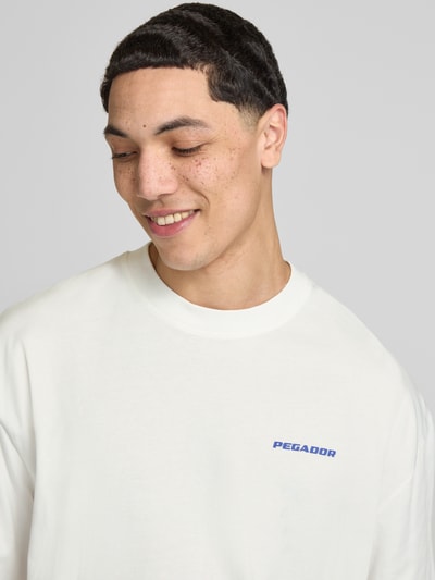 Mężczyznamodel nosi Oversized T-Shirt mit Label-Detail Modell 'Bovec' von Pegador z bawełny, krój oversized fit, okrągły dekolt, detal z logo, długość tyłu w rozmiarze M: 71 cm, jasny kolor, gładka tekstura, z przodu logo, zbliżenie na górną część ciała