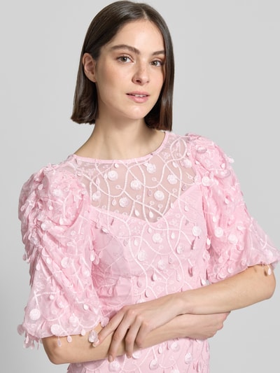 Kobiece model prezentuje wieczorową sukienkę z aplikacjami model 'BEATE' od YAS, różowy kolor, bufiaste rękawy, zbliżenie tułowia. Szerokość w rozmiarze S: 36 cm, długość tyłu: 145 cm, długość rękawa: 38 cm, krój dopasowany, dekolt w serek z przodu i z tyłu, tekstura ażurowa.