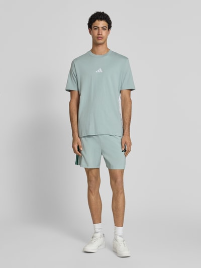 Männermodel trägt Regular Fit T-Shirt aus reiner Baumwolle von adidas Sportswear, Optik: Unifarben, Logo-Stitching, Kontraststreifen, Rundhals, Kurzarm, Ganzkörperansicht von vorne.