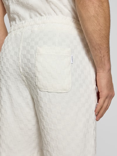 Männermodel trägt Regular Fit Shorts mit Label-Patch von Lindbergh, weiße Baumwoll-Mix Textur, Detailaufnahme Rückansicht.
