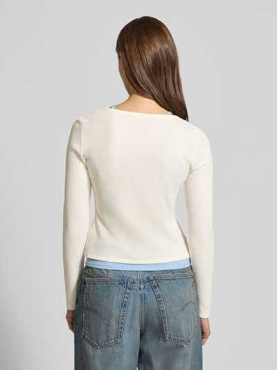 Frauenmodel trägt Slim Fit Longsleeve mit Strukturmuster von Guess Jeans in Offwhite mit Layered-Look, Elastischer-Material-Mix, Rückenlänge 47 cm, Ganzkörperansicht Rückansicht.