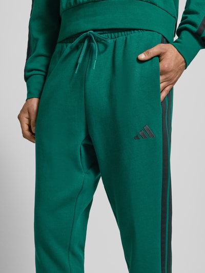 Männermodel trägt grüne Sweatpants mit elastischem Bund von adidas Sportswear aus Baumwoll-Mix mit Viskose-Anteil, Nahaufnahme Oberkörper.