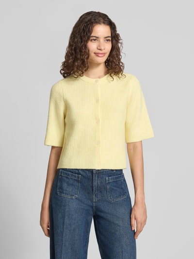 Frauenmodel trägt Boxy Fit Strickjacke aus Rippstrick Modell 'SILLY' von PIECES in Gelb, melierte Optik, Crew Neck, Kurzarm, Ganzkörperansicht von vorne.