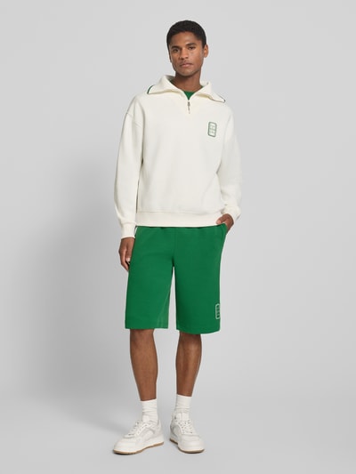 Mężczyzna model nosi Loose Fit Troyer aus Baumwoll-Mix Model 'Tennisc' od Lacoste, białe i zielone tony, gładka tekstura, całkowity widok z przodu, Herren troyer od Lacoste.
