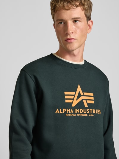 Männermodel trägt Regular Fit Sweatshirt aus Baumwoll-Mix mit Logo-Print von Alpha Industries in Dunkelgrün, Nahaufnahme Oberkörper.