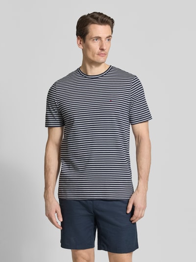 Männermodel trägt Regular Fit T-Shirt aus reiner Baumwolle von Tommy Hilfiger, gestreift, Logo-Stitching, Rundhals, Ganzkörperansicht von vorne.
