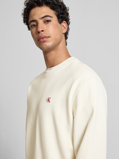 Męski model nosi Sweatshirt aus reiner Baumwolle od Calvin Klein Jeans w kolorze ecru, okrągły dekolt, proste rękawy, widoczne logo, zbliżenie na górną część ciała.