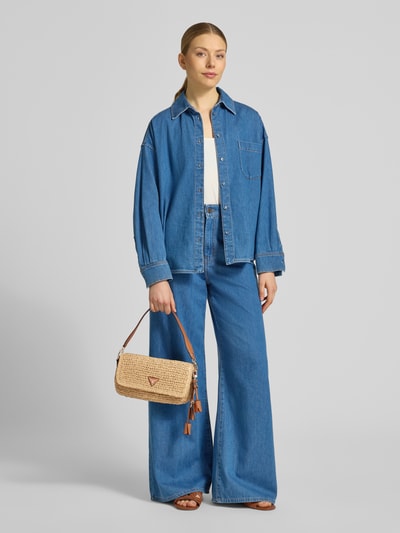 Kobiece modelka nosi torba na ramię Shoulder Bag in Flecht-Optik model 'OFELIA' od Guess w kolorze beżowym z detalem z logo, główna przegroda z klapką, odpinany pasek na ramię, zapięcie na magnes, kieszeń wewnętrzna na zamek błyskawiczny, szerokość w rozmiarze 1: 28 cm, długość w rozmiarze 1: 16 cm, głębokość w rozmiarze 1: 6 cm, długość paska na ramię w rozmiarze 1: 130 cm, efekt plecionki, widok całej sylwetki z przodu.