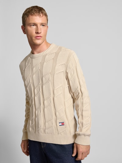 Männermodel trägt Regular Fit Strickpullover aus reiner Baumwolle von Tommy Jeans, Optik: Unifarben, Strickoptik, Zopfmuster, Logo-Detail, Rundhals, Langarm, Ärmelabschluss und Rumpfabschluss gerippt, Material: Baumwolle, Ganzkörperansicht von vorne.