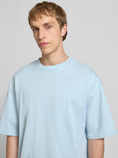 Mężczyzna model nosi Oversized T-Shirt mit Logo od REVIEW, jasnoniebieski, czysta bawełna, szeroki krój, logo, dekolt okrągły, Nahaufnahme górnej części ciała.