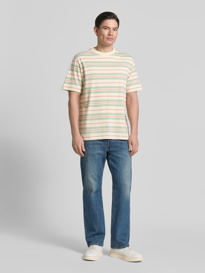 Männermodel trägt Relaxed Fit T-Shirt aus reiner Baumwolle Modell 'MAARKOS' von Armedangels, gestreift, mehrfarbig, Ganzkörperansicht von vorne.
