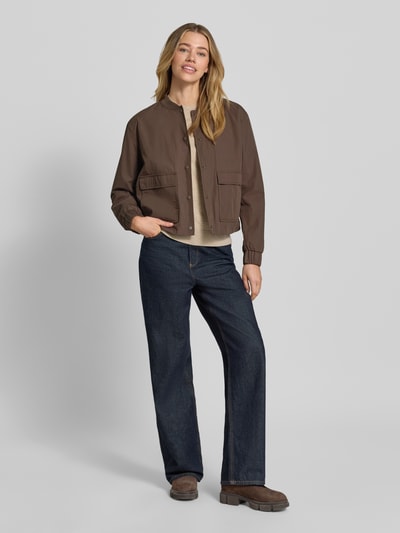 Kobiece modelka nosi Jacke mit Pattentaschen von camel active, mieszanka bawełny, krój regular fit, stójka, listwa guzikowa, kieszenie z patką, długość tyłu w rozmiarze 36: 54 cm, szerokość ramion w rozmiarze 36: 43 cm, szerokość klatki piersiowej w rozmiarze 36: 55 cm, długość rękawów w rozmiarze 36: 58 cm, ciemne i beżowe kolory, proste kształty, gładka faktura, całopostaciowe ujęcie z przodu.